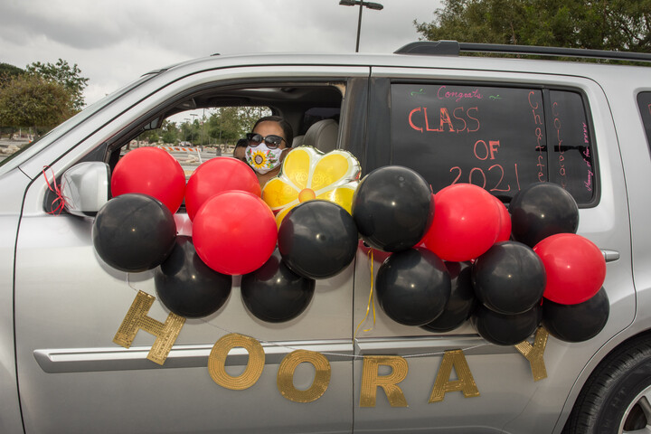 Graduate student driving a vehicle decorated with red, yellow and black balloons.