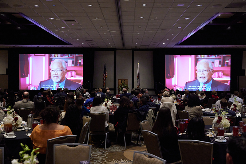 Report to the community attendees watching a featured video of student success stories.