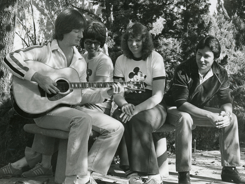 1980s student playing a guitar with his friends