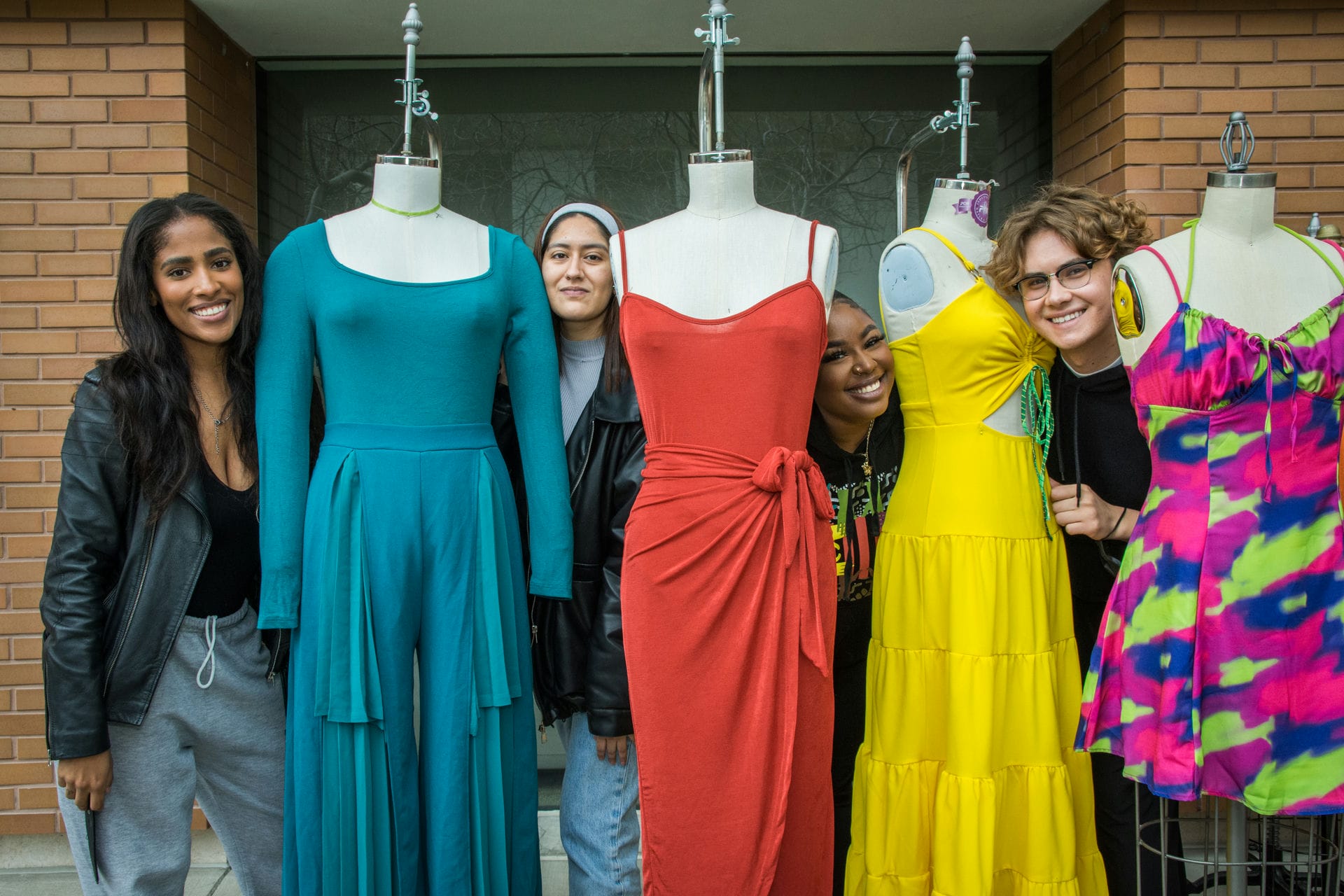 Fashion students standing between female mannequins in elegant cloths.