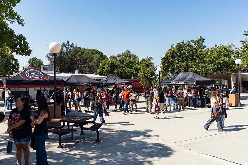 An outdoor Chaffey College event features students mingling around black tents