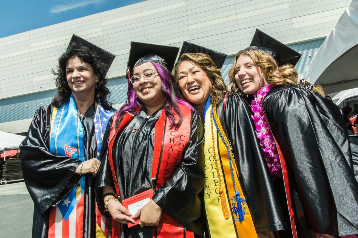 Four women in graduation caps and gowns smile brightly. Sashes read CHAFFEY COLLEGE, and one woman wears a pink lei.