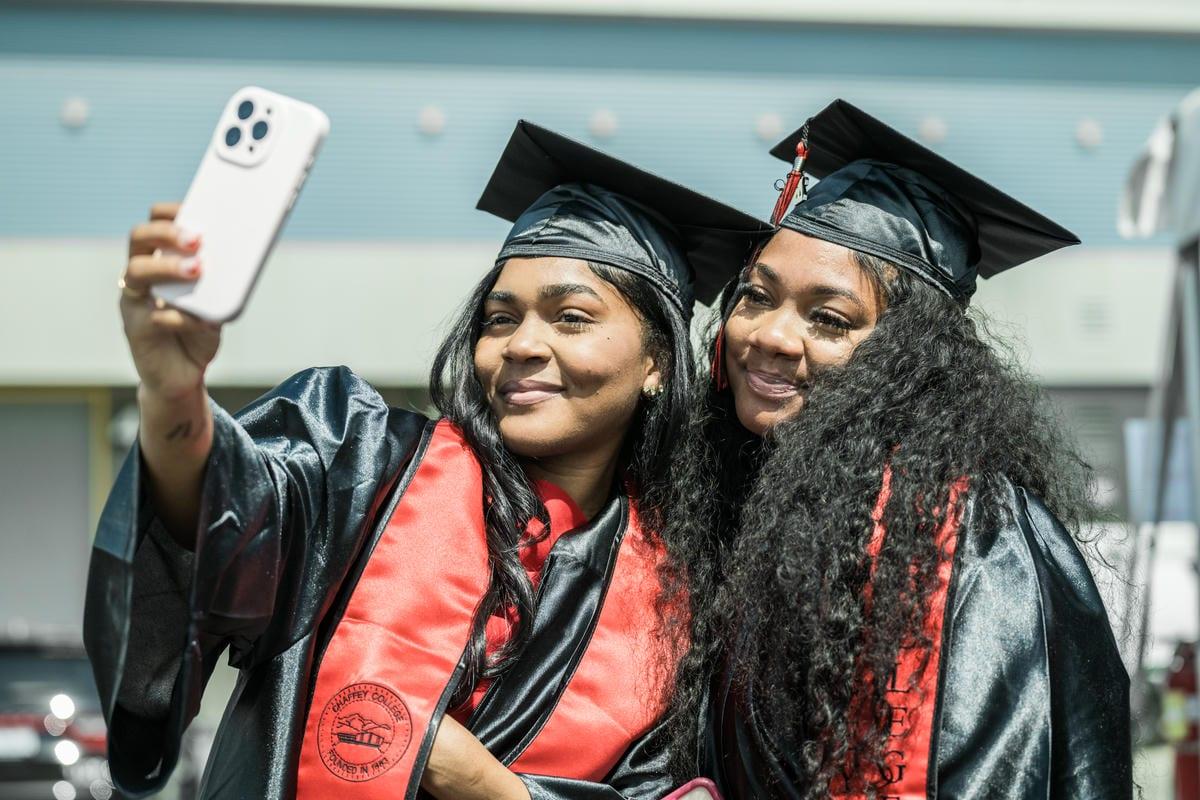 Two smiling Chaffey College graduates, dressed in caps and gowns, capture a selfie. Their red stoles read CHAFFEY COLLEGE, FOUNDED IN 1883.