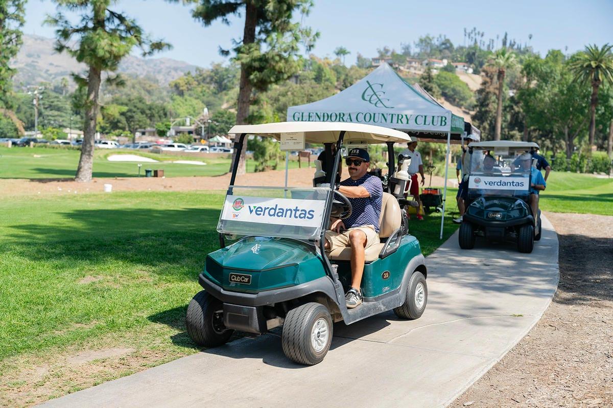 A golfer drives a green cart past the Glendora Country Club event tent, followed by a second cart.