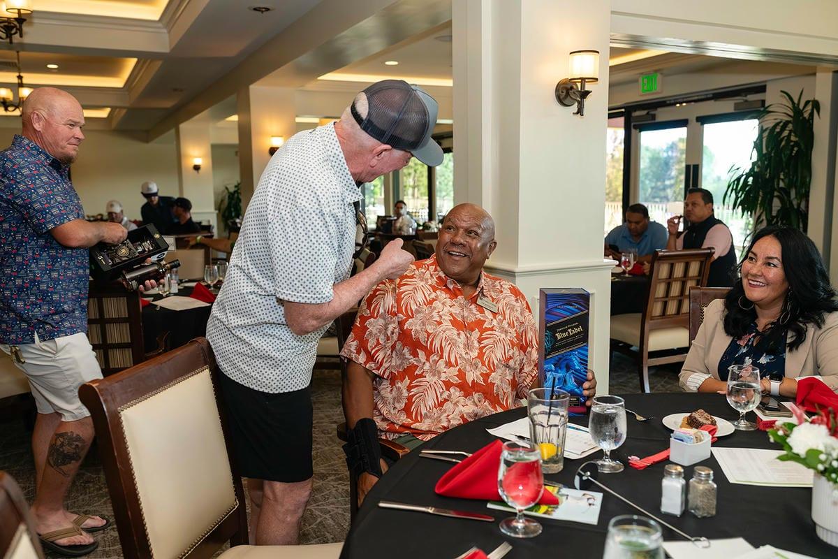Guests smile and converse around a banquet table during the golf tournament’s indoor reception.