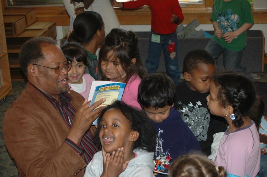 Dr. Shannon sits on the floor reading a book aloud to children at the children's center