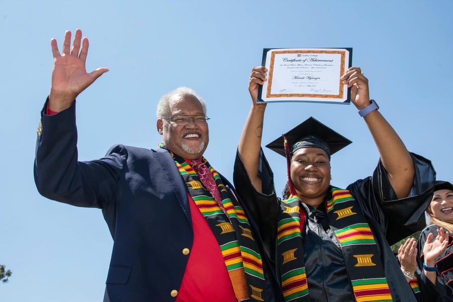 Dr. Shannon waves with graduate holding diploma above their head at Chaffey College commencement ceremony in 2022.