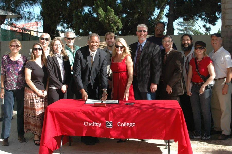 Dr. Shannon smiles as he signs paperwork surrounded by a group during his president's commitment signing.