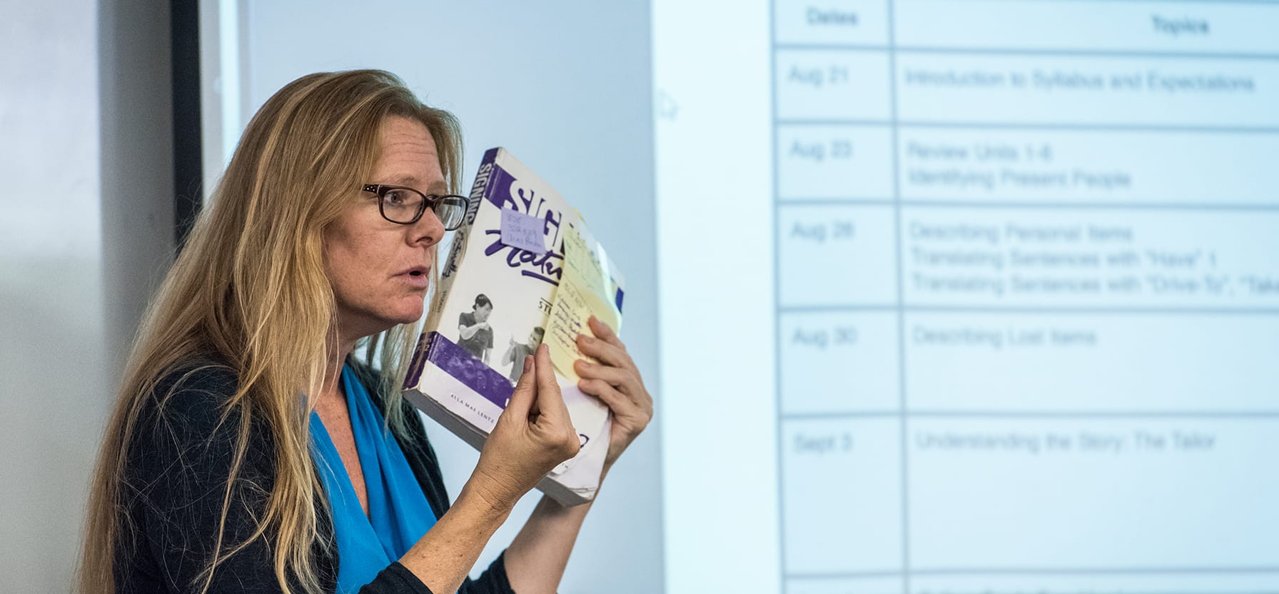 An American Sign Language instructor demonstrates sign language in front of a class.