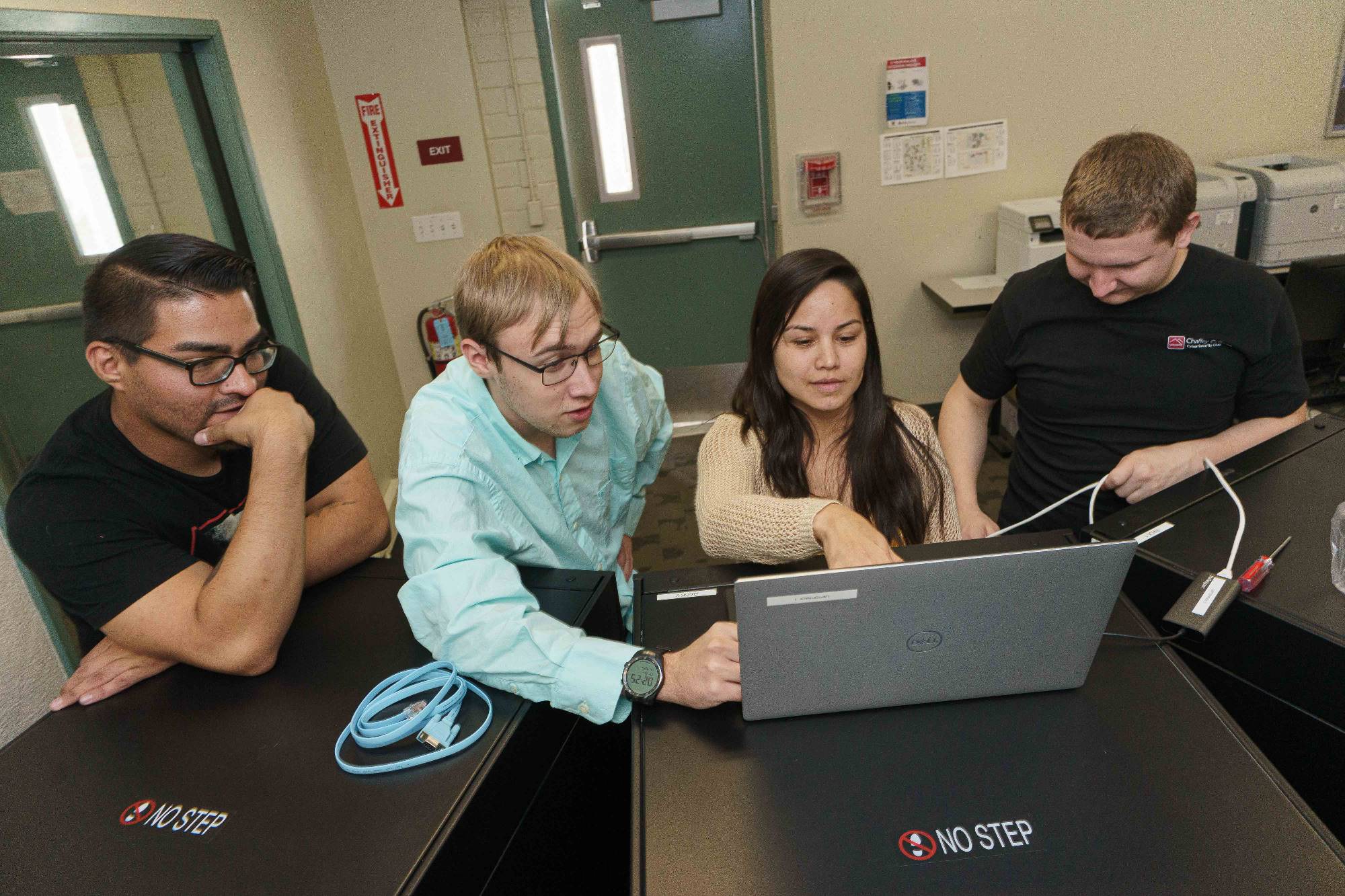 Cybersecurity students examine a laptop during a class.