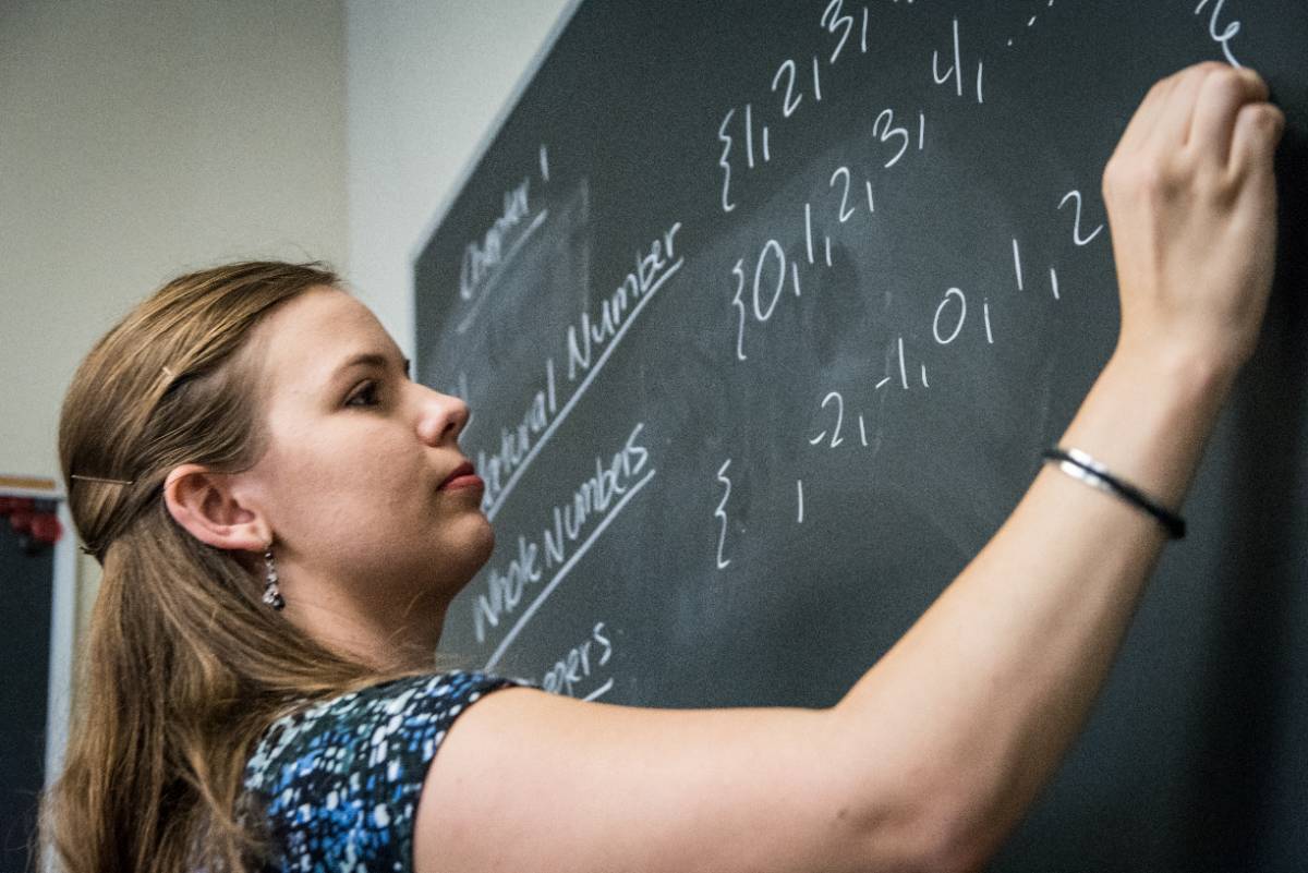 A professor writes numbers on a board.