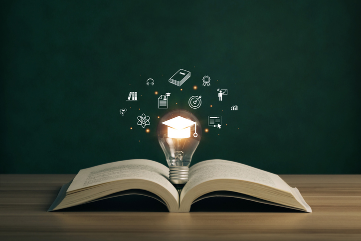 An open book with a glowing lightbulb, featuring a graduation cap and educational icons