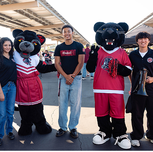 Four students pose with two panther mascots outdoors.