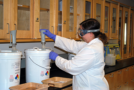 A member of the Chemistry staff dispenses chemicals from a properly labeled container.