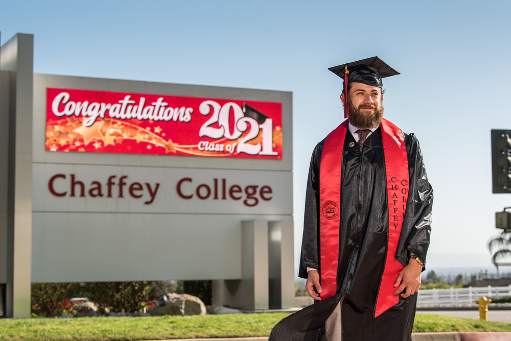 David Leon, wearing a graduation cap and gown, poses in front of the Chaffey marquee