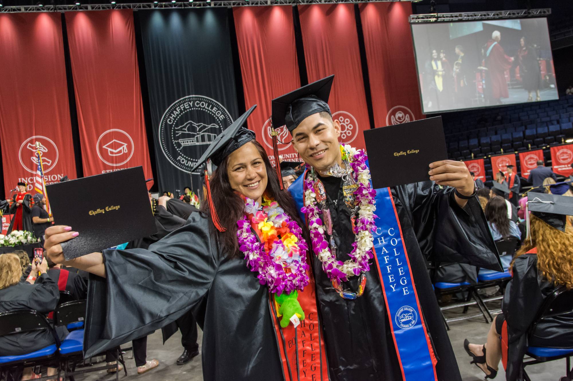 A mother and son graduating from Chaffey hold up diplomas