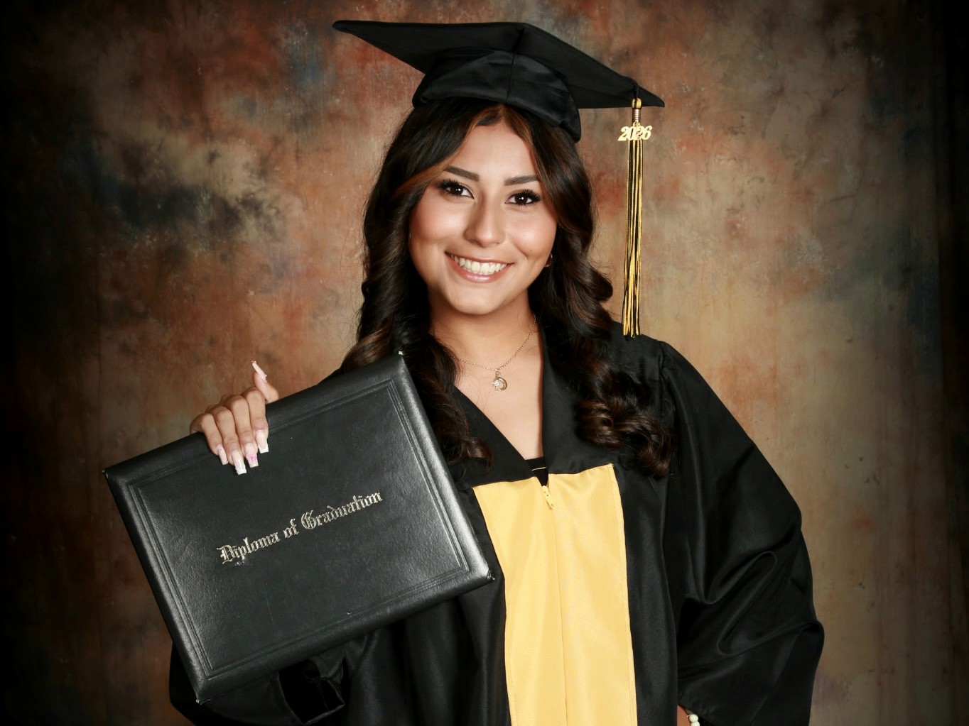 Hailey Contreras wears a graduation cap and gown and holds up a diploma
