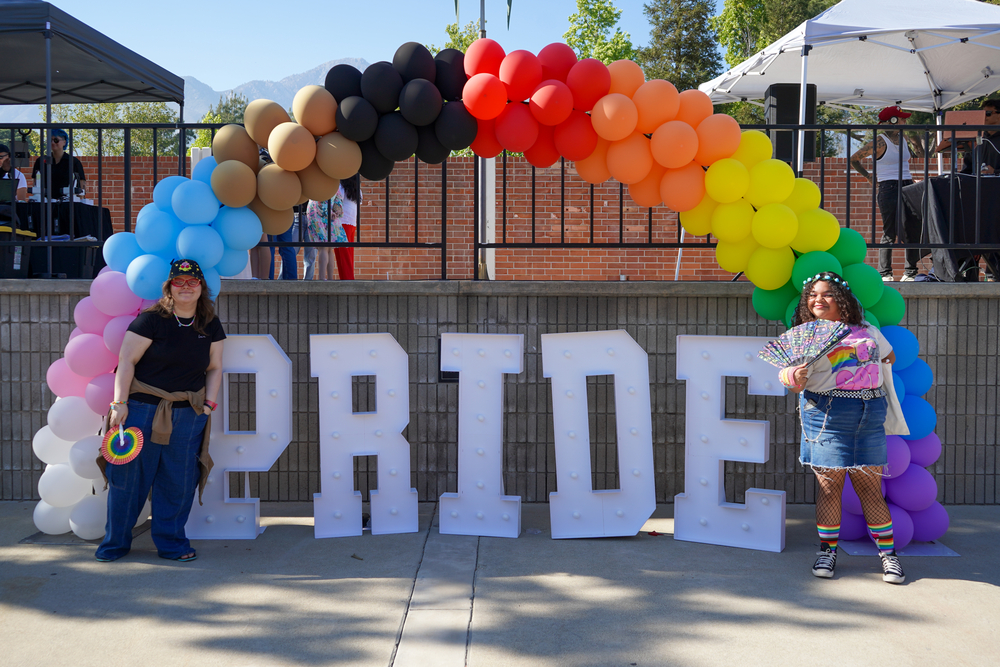 Two guests pose by Pride Fest sign and rainbow balloons.