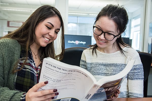 Two smiling Chaffey College students work together reviewing a large textbook.