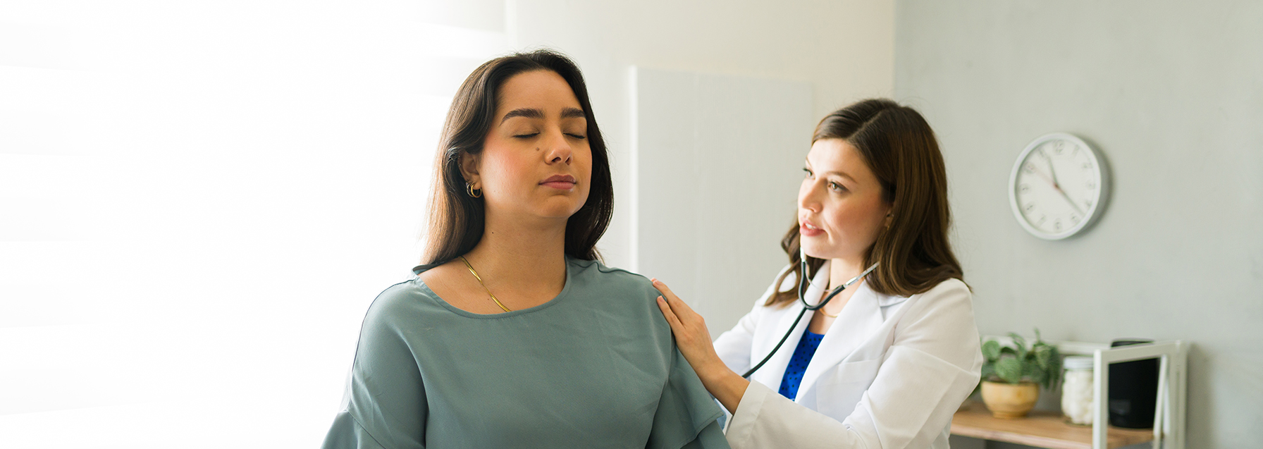 Female Hispanic patient inhaling while her doctor is listening to her breathing during a medical consultation - stock photo
